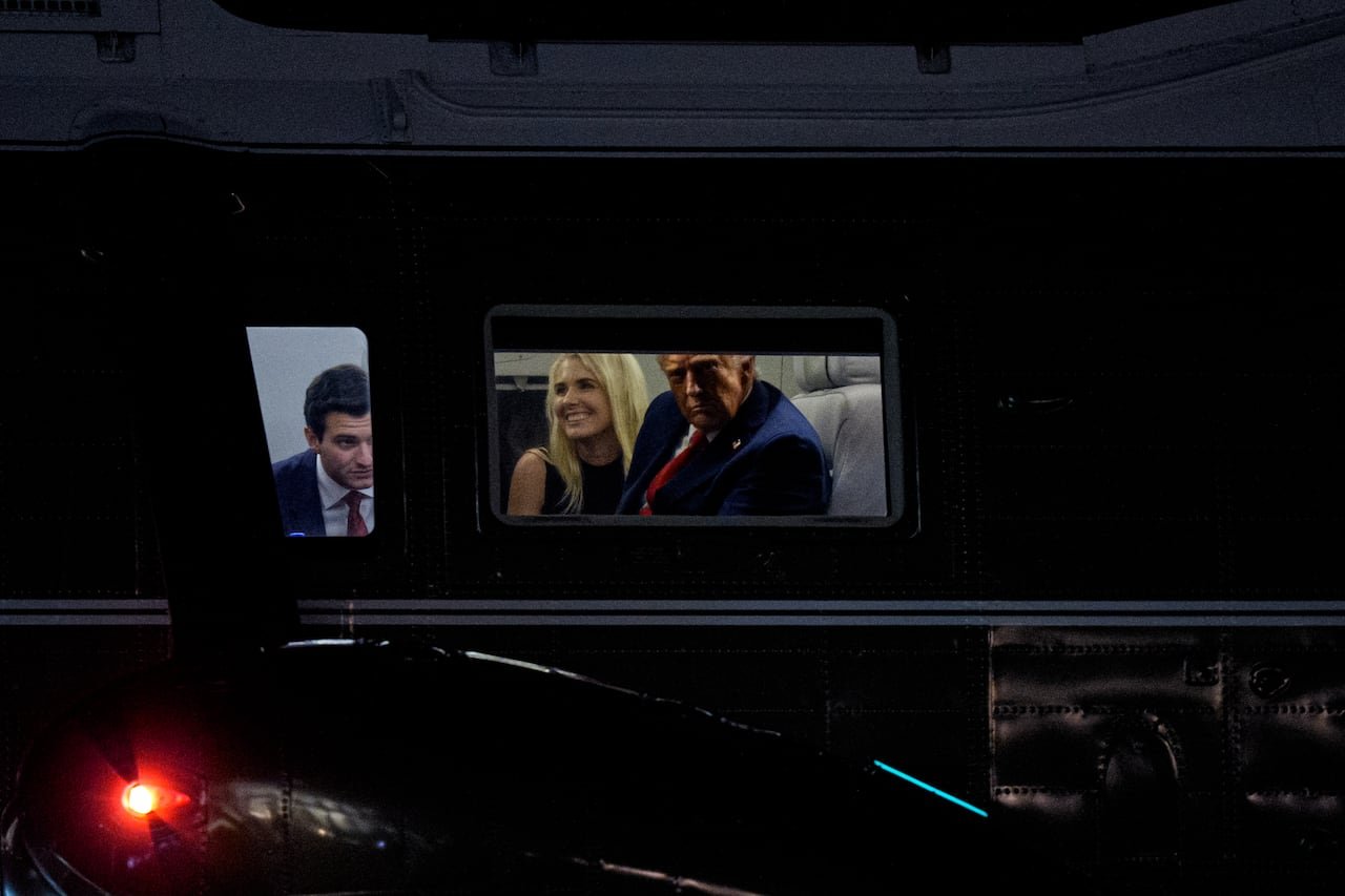 default-112 Two men in suits and a smiling woman with shoulder-length blonde hair are illuminated through a window, with darkness outside.