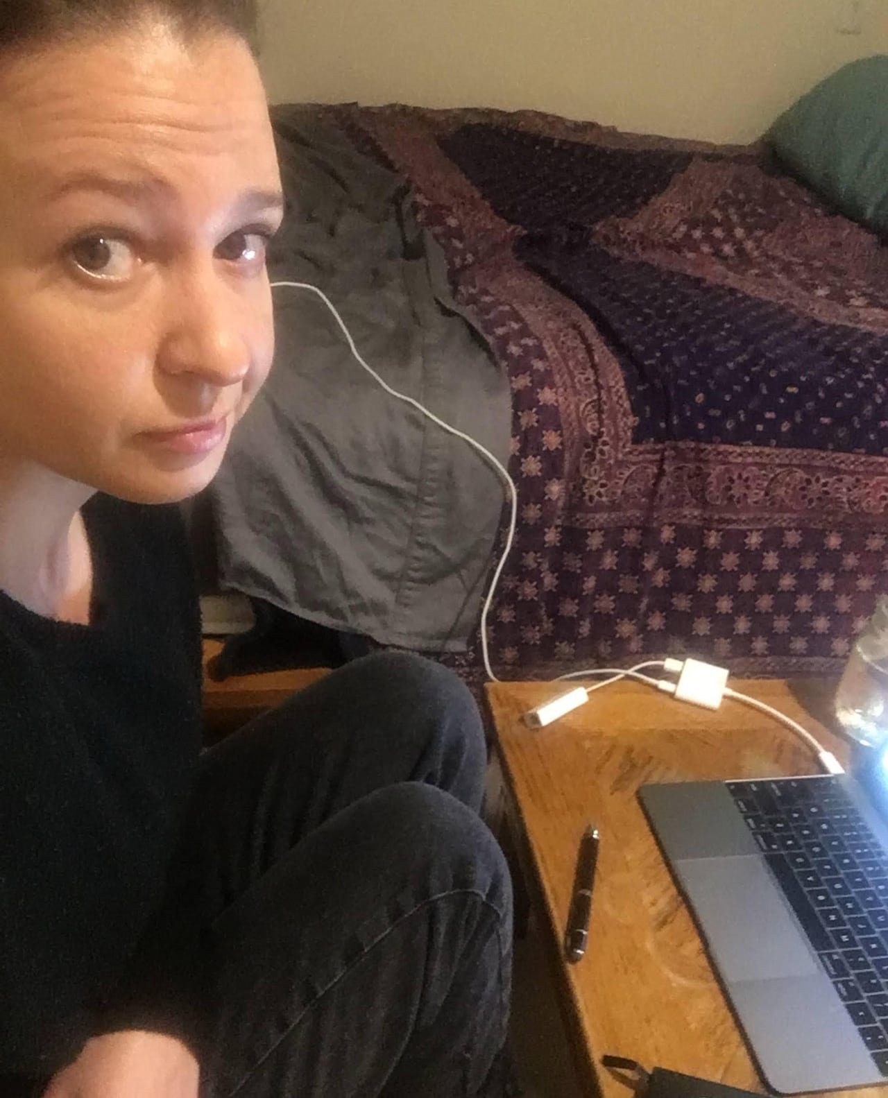 default-17 A woman poses for a selfie while sitting next to her laptop and bed.