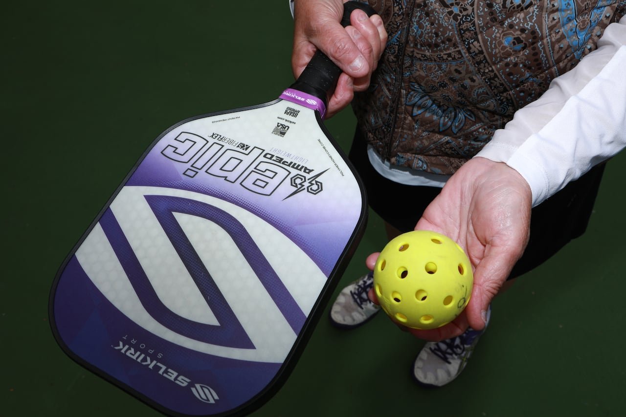 Close up photo of a pickleball paddle and ball in a woman's hands.