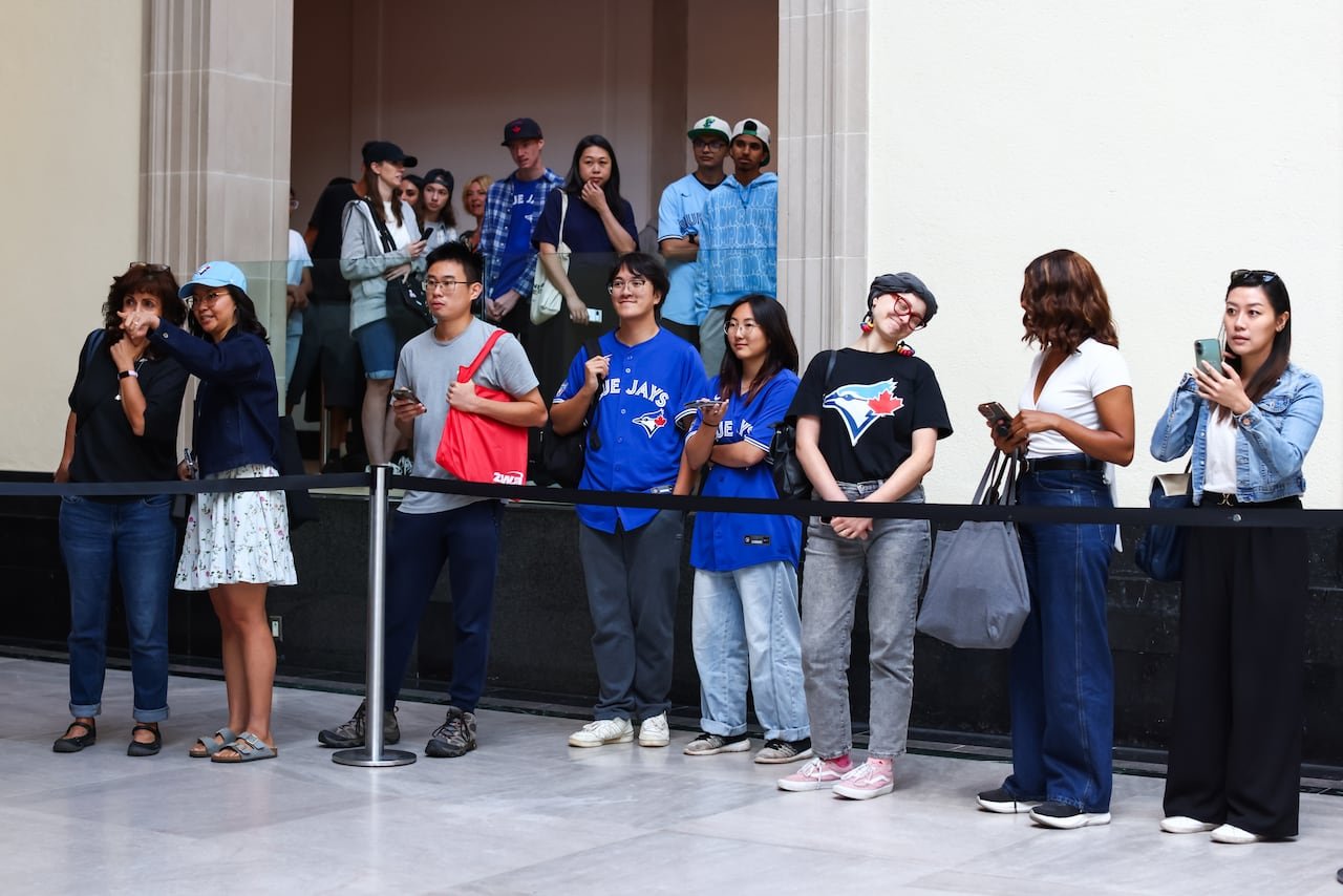 default-42 Eight individuals standing in a row behind a black line adorned in Blue Jays merchandise.