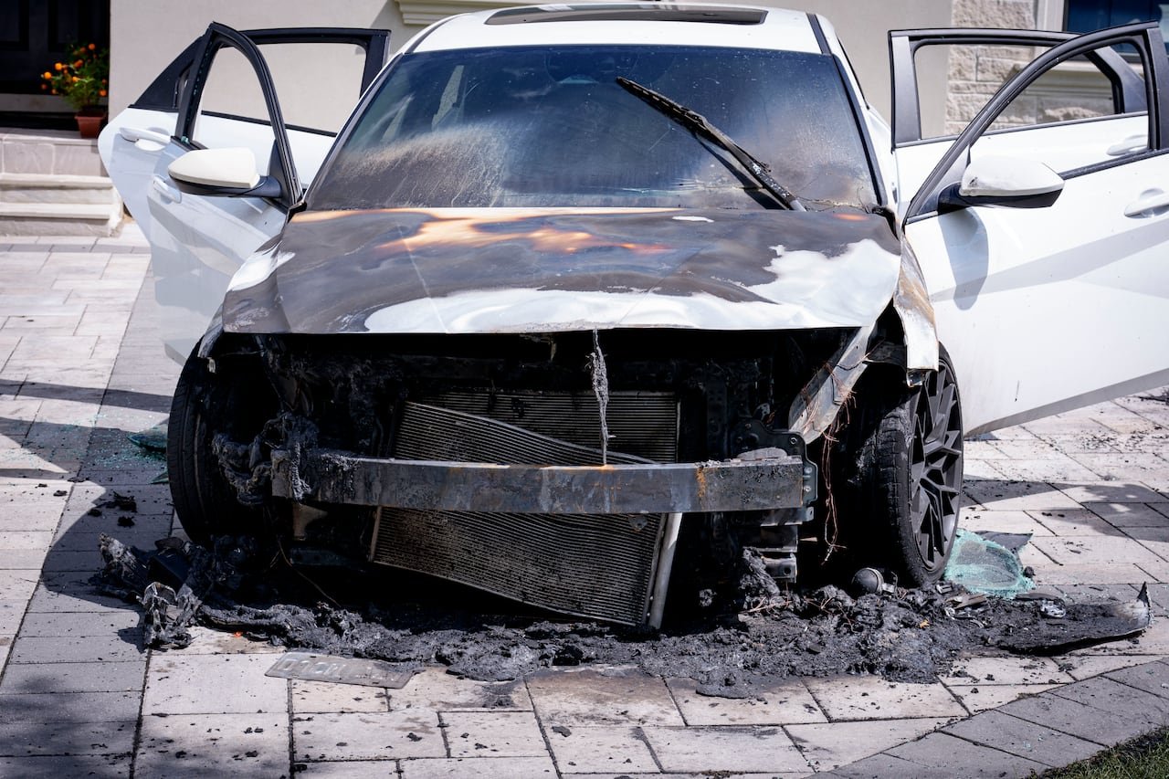 Close-up of a burned white car with damaged front bumper and debris scattered.